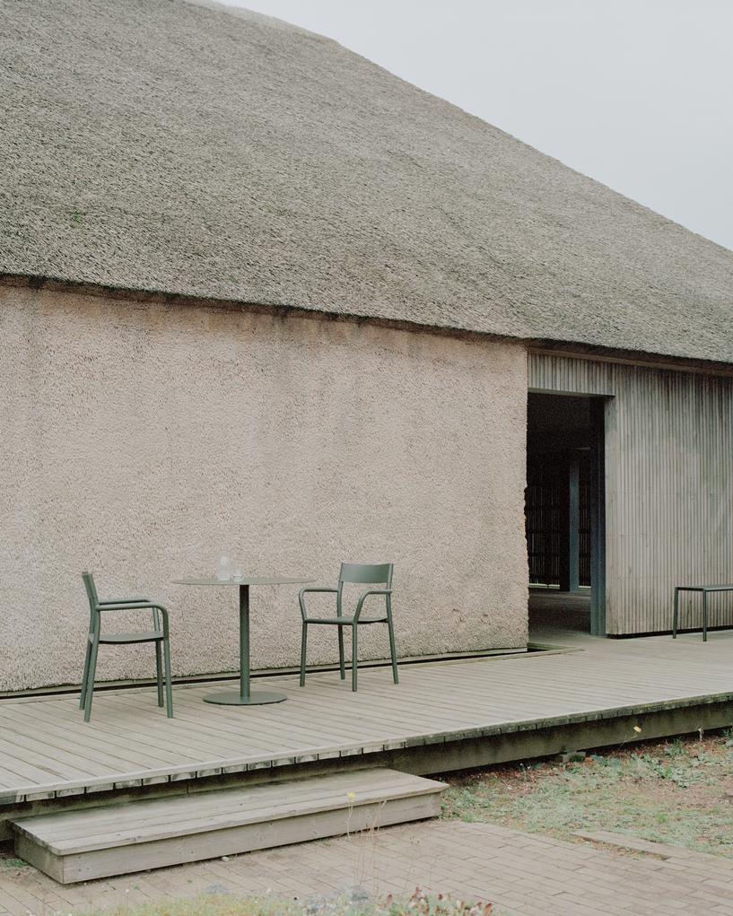 Modern outdoor setting with a thatched roof building, wooden deck, and green chairs.